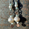 Each earring has two sections. The lower has a large white bead with a smaller pale blue bead above and below, all strung on copper wire with a neat spiral at the bottom. This is linked to a piece with pale blue beads above and below a white bead that's scarcely larger, all strung on steel wire that curves back up around each bead, then twists around itself.