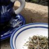A blue and white teapot sits on a saucer; next to it a small plate holds about enough looseleaf tea for a single mug.