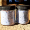 Two clear glass jars are filled with pale blue bath salts.