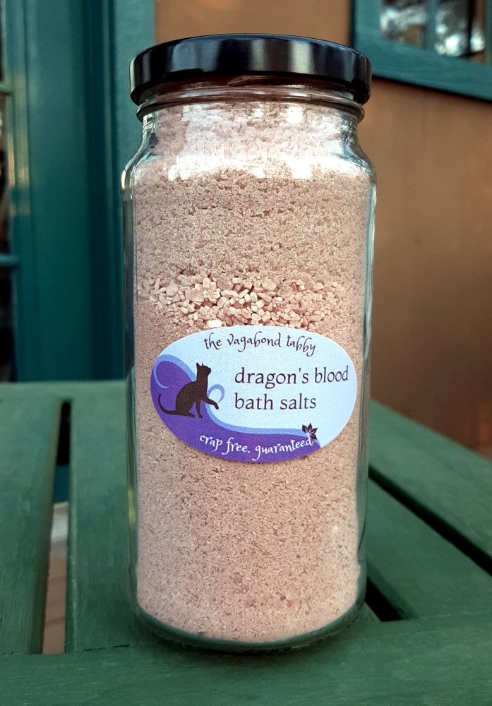 A tall, clear glass jar filled with reddish-brown bath salts.