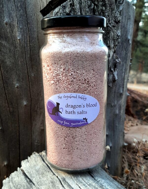 A tall, clear glass jar filled with reddish-brown bath salts.