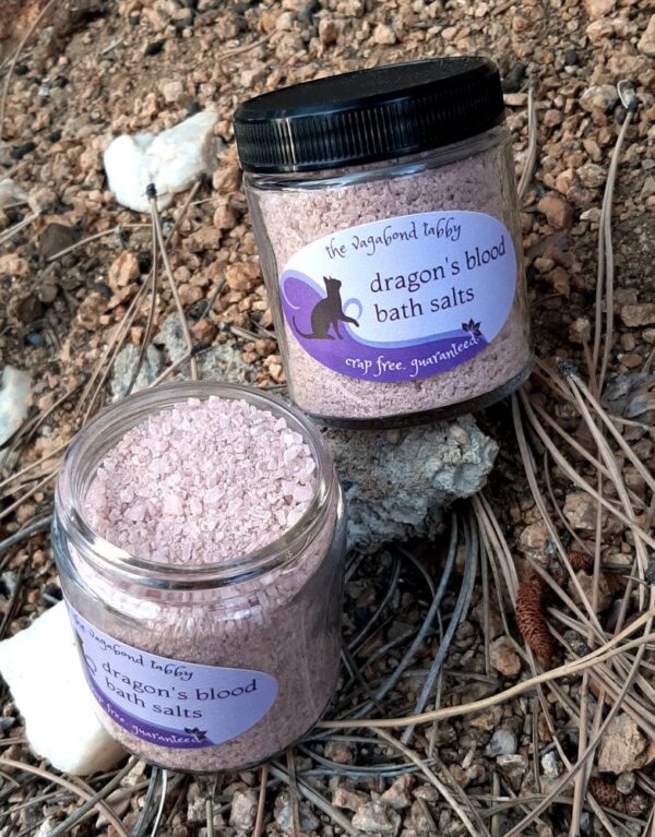 Two clear glass jars filled with reddish-brown bath salts. One has been opened to show the bath salts inside.