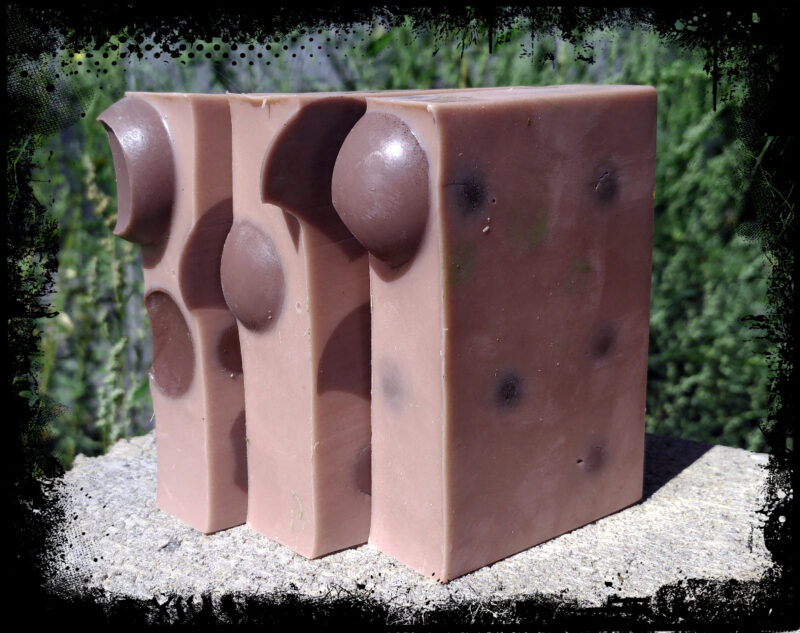 Three bars of soap, medium brown with dark brown spheres embedded in them.