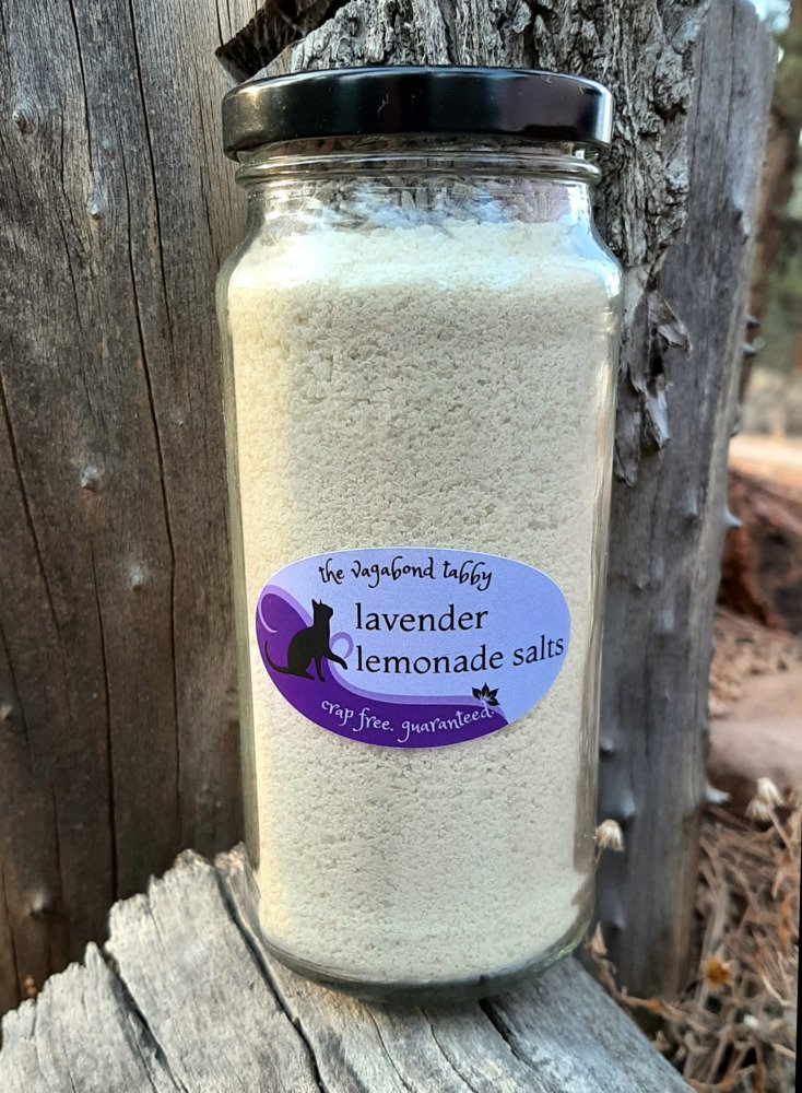 A tall, clear glass jar filled with yellow bath salts. A layer of lavender is just visible at the top.