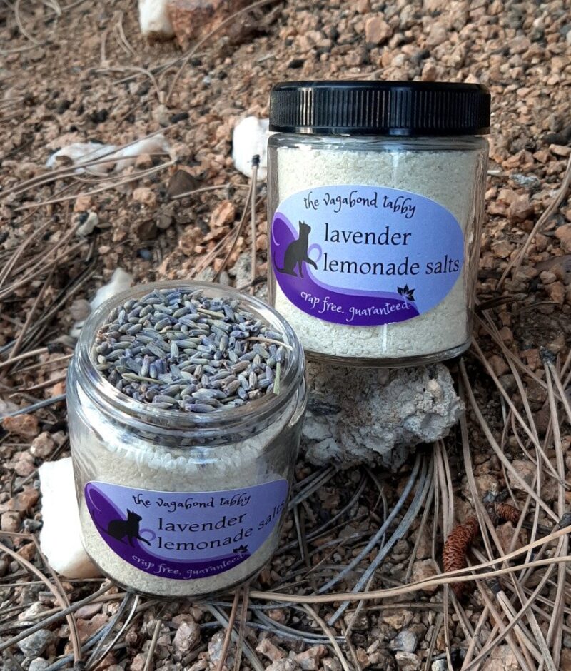 Two clear glass jars filled with yellow bath salts. One is open, showing the layer of lavender at the top.