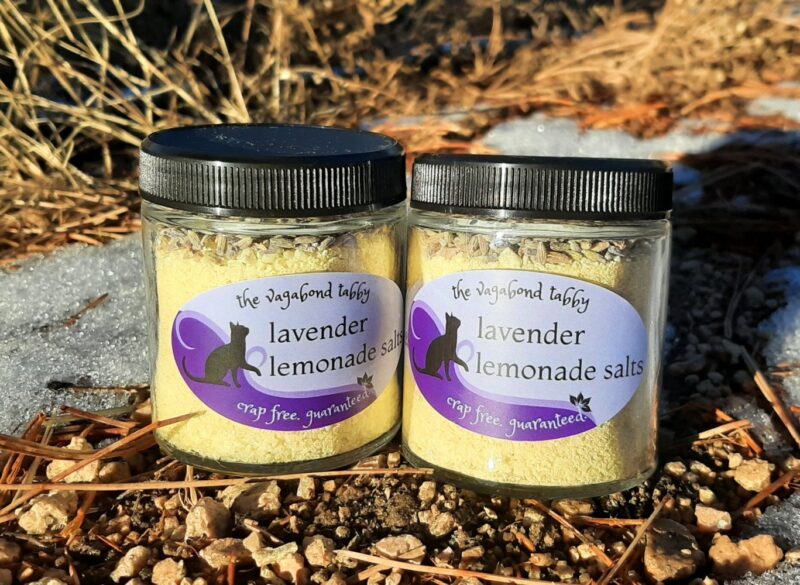 Two clear glass jars filled with yellow bath salts. A layer of lavender is just visible at the top of each.