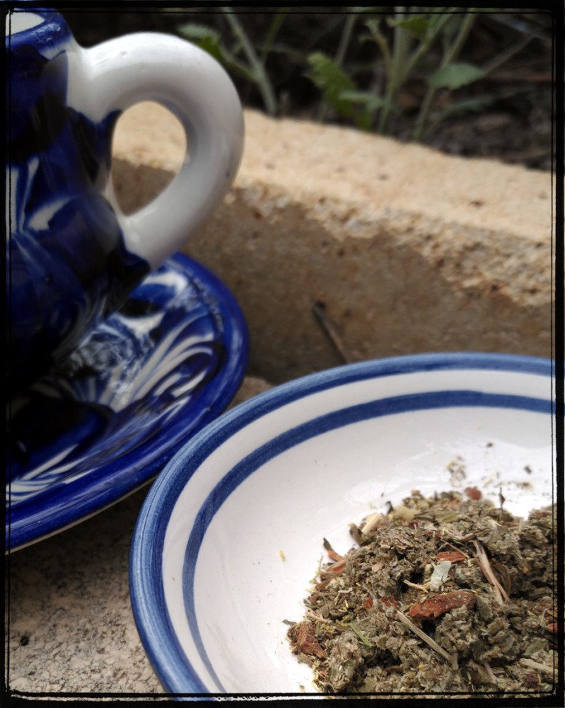 A blue and white teapot sits on a saucer; next to it a small plate holds about enough looseleaf tea for a single mug.