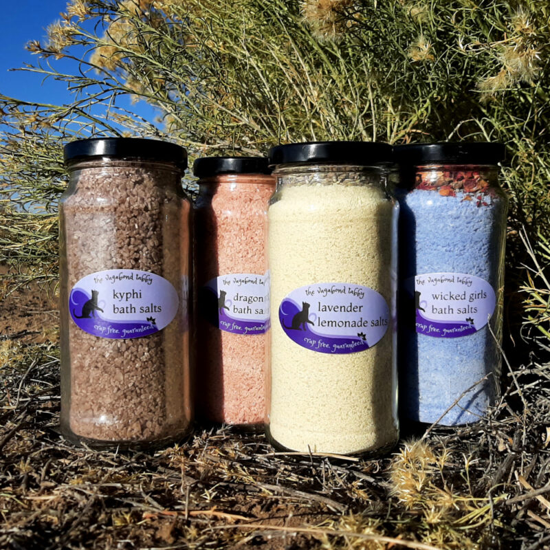 Four tall, clear glass jars of bath salts. One jar holds brown bath salts, the next red; the third is yellow and the fourth, blue.