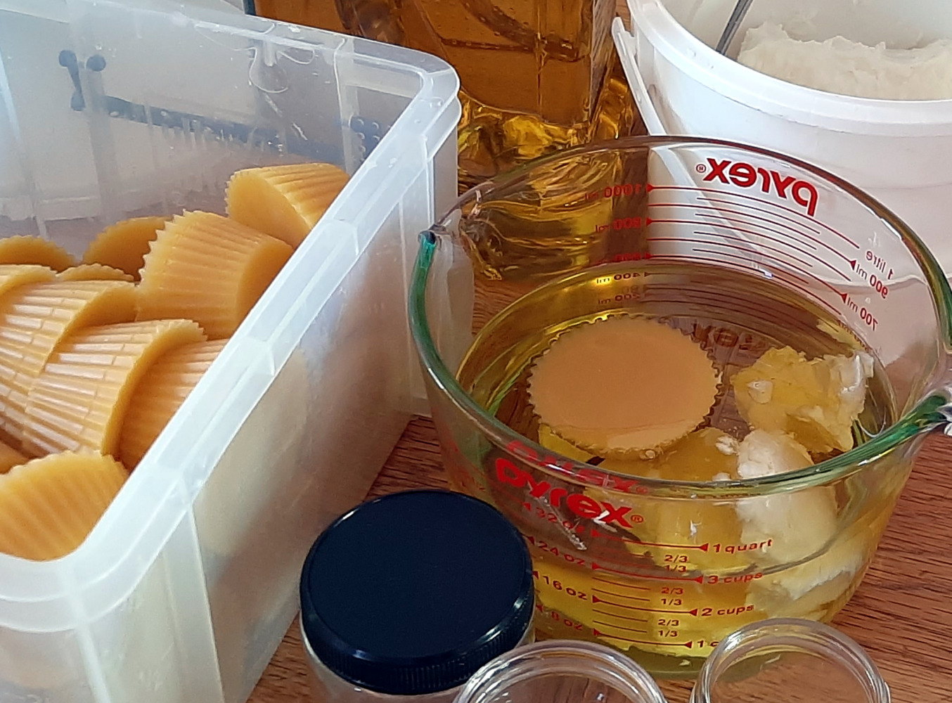 Three salve jars, all empty, sit next to a plastic bin filled with cupcake-shaped hunks of beeswax. A big glass mixing bowl holds another chunk of beeswax, along with olive oil and three lumps of white shea butter.