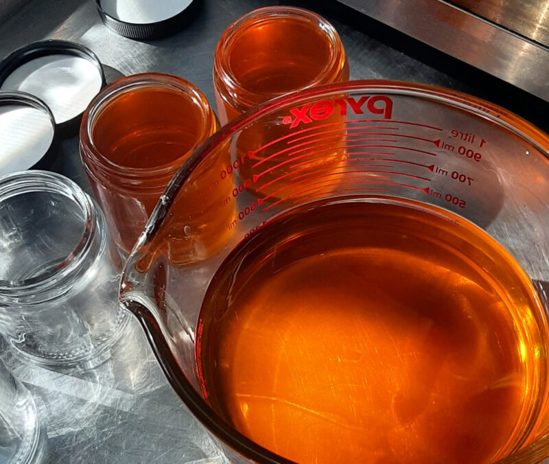 Two glass salve jars and a big glass mixing bowl, all filled with golden-orange salve, sit next to a third empty jar. Three lids sit just beyond the jars.