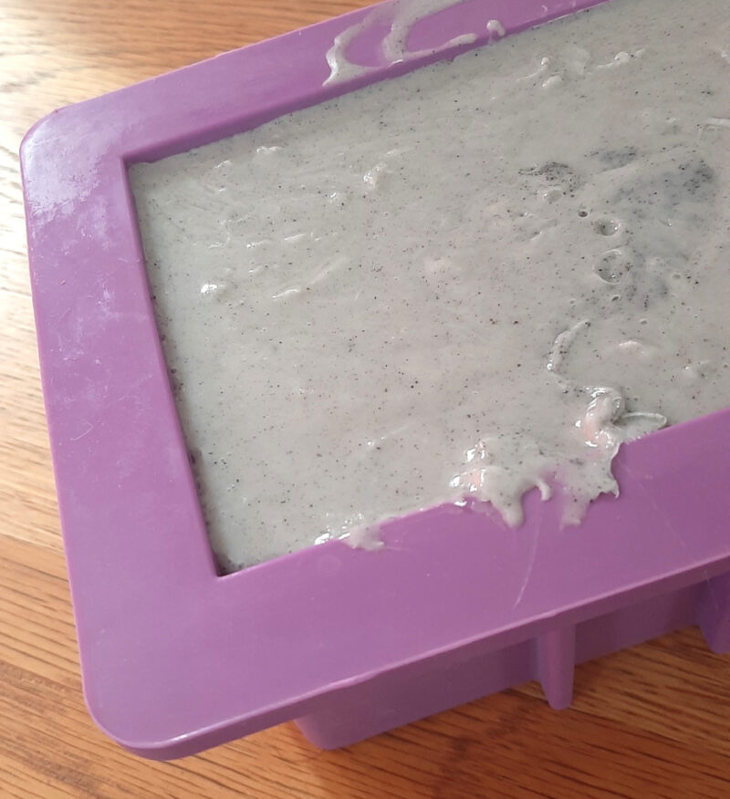 A purple soap mold is filled with pale blue-grey soap.