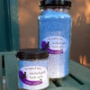 Two clear glass jars filled with blue bath salts. The very top of the taller one holds a layer of rose petals.