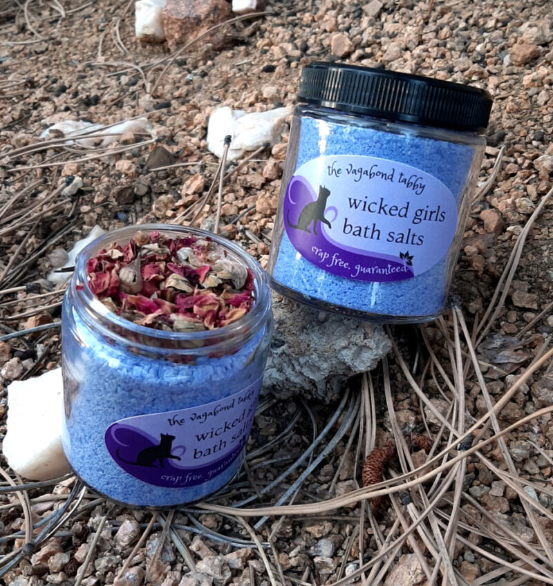 Two clear glass jars filled with blue bath salts. One is open, showing that the top of the jar is filled with rose petals.