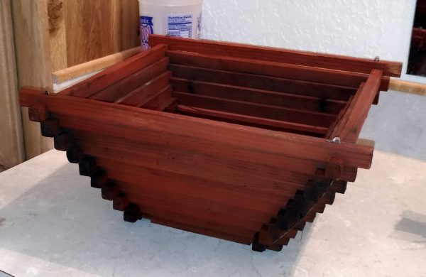 A wooden plant pot, in the shape of an upside-down step pyramid. It's wood, stained dark red.