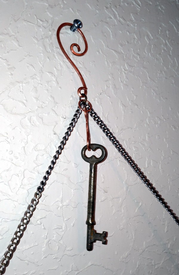A closeup of the hook holding the chain that the duck stick hangs from. It's looped copper wire, with another skeleton key hanging below it.