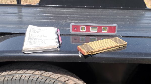 On the thing that goes over the tires on the trailer, there's a notepad with pink pen, a short carpenter's level, & an old-fashioned folding carpenter's ruler.
