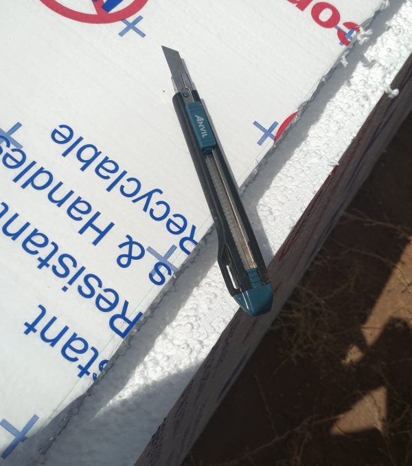 A box cutter sitting on top of foamboard insulation, which has been broken along a straight line.
