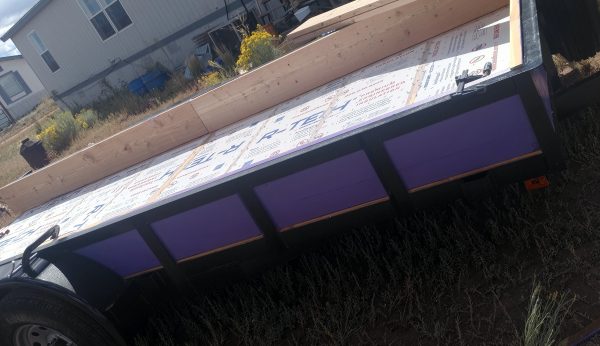 The trailer, seen from the side. The boards of the box are visible between the upright shafts of the railing. The purple looks pretty cool against the black railing.