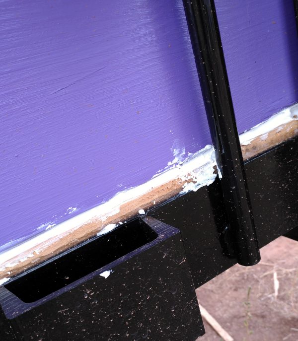 There's a big purple-painted board above, a thin unpainted board below, & a really messy line of caulk in between.