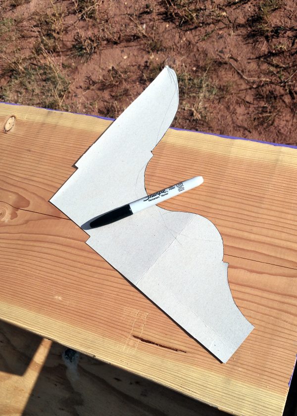 A white piece of cardoard with a sharpie sitting on it. The shape is two straight edges at right angles, with the third side curved in a decorative fashion.