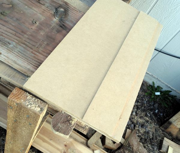 Sitting on top of the board, neatly aligned with it along the bottom, is a piece of fiberboard with a narrower piece of fiberboard sitting atop it.