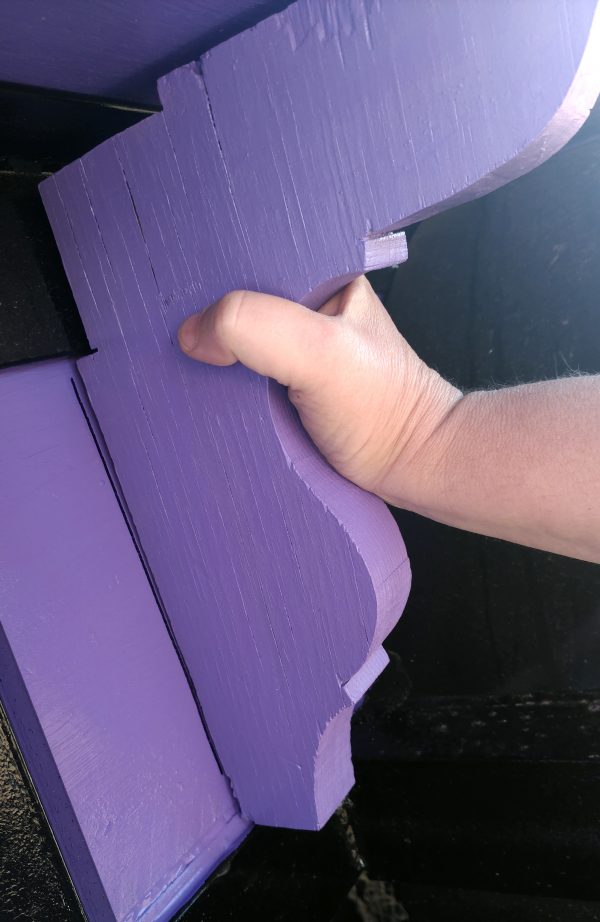 One of the braces, painted entirely purple & held in place on the side of the tinker's wagon by my hand.