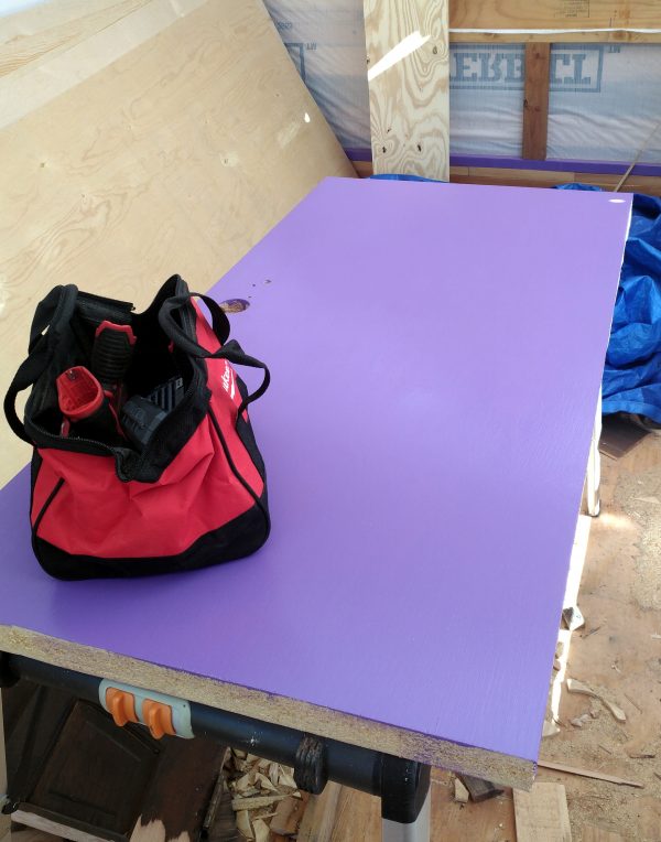 A door lays on a table in the middle of the tinker's wagon. It's vigorously purple, & there's a red toolbag sitting on it.