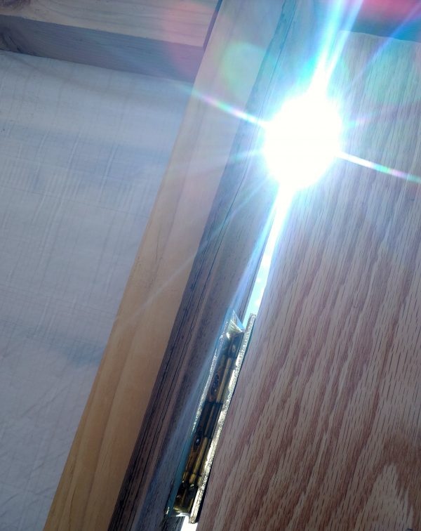 The door from the inside again, close up on the gap where the hinges are. The sun is shining brightly through the gap in a way that recalls a Michael Bay lens flare. DRAMATIC