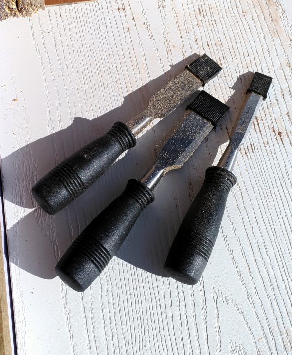 Three wood chisels of varying widths lay on a white tabletop.