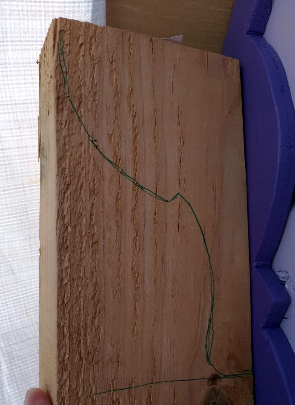 I'm holding a hunk of 2x4 up to the corner of the roof. An outline reminiscent of the shelf supports is traced on it in green, but the 2x4 sticks out past the end of the roof by more than an inch.