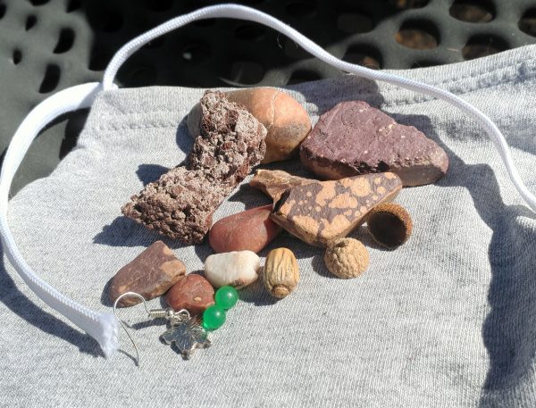 An acorn cap, two small bright green plastic balls, a single silver butterfly earring, & a pile of good rocks sit on a pouch sewn from grey t-shirt fabric with a shoestring for a drawstring.