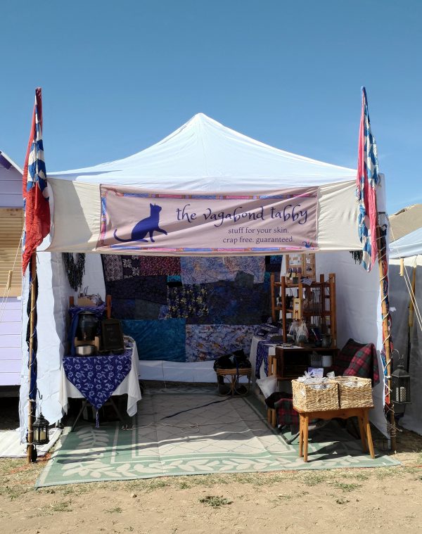 Red, white, & blue banners (but not American flags) fly on either side of the booth. Within, a crazy quilt in blues & purples covers the back wall. A table stands along each side wall, each filled with treasures.
