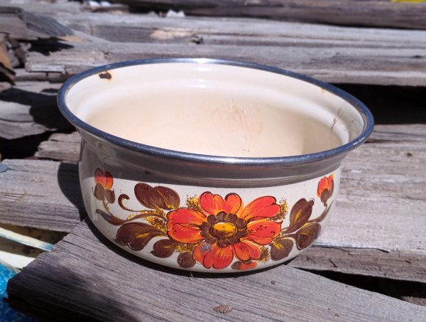 A small cooking pot, enameled in white with an orange flower & brown leaves painted on the side. Very 70s.