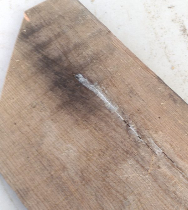 A pretty blurry close view of a rough plank with white glue drying in some of the larger cracks.