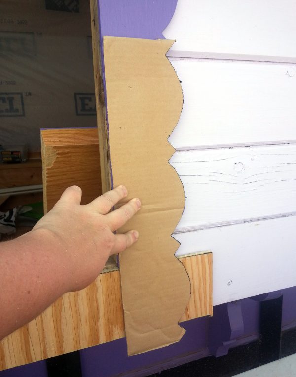 My hand, holding the template with the trim pattern on it up to the right side of the piece of bottom trim.