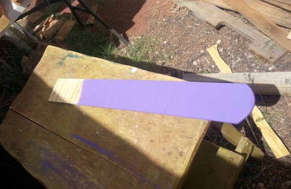 A piece of plywood, four inches wide & a couple feet long, one short end cut into a curve. It's sitting on a table in the sun, & most of it has been painted purple.