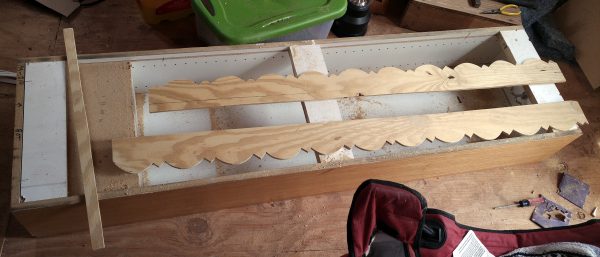 Most of the back of the cabinet has been cut away, except for small sections at the top, bottom, & middle, enough to keep it stable. Two pieces of cut trim have been laid across it.