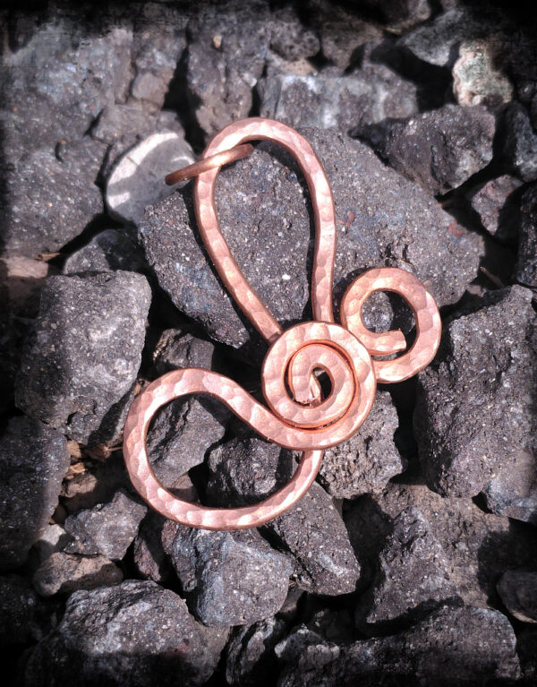 Overlapping spirals in hammered copper are joined by a pair of arching curves, one rising upwards, the other ducking slyly off to the left.