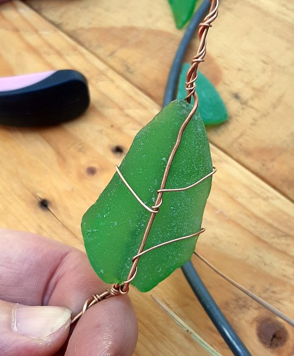 In my hand: a leaf-shaped piece of green seaglass. It is wrapped in copper that follows where a leaf's veins might go.