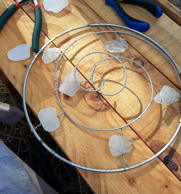 There are now six seaglass pieces fastened in the spaces between the spiralling wire. The thicker wire is in sort of a double loop at the center, because the spiral isn't quite the same shape it was before. I don't know how to describe it right, words are hard.
