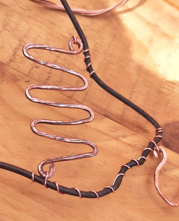 One of the zigzag pieces has been attached to the clothes hanger wire by thinner copper wire that winds through the loop at each end several times, & then around the clothes hanger wire.