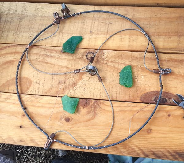 The ends of each length of cable have been attached, with copper wire, to the three bumps in the round bit. The piece that joins them sits at the center, so they make sort of a bumpy triskele. A piece of green seaglass sits inside each section.