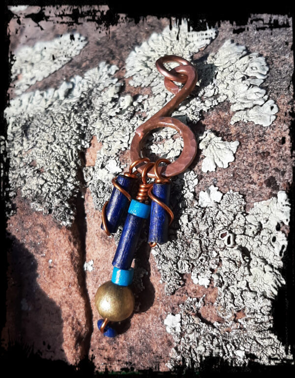 Thick copper wire bent into the shape of a music note. Three strands of beads, in dark blue, teal, and brass, hang from the bottom curve.