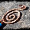 A spiral of hammered copper wire. Two lengths of thinner copper wire, threaded with blue and tan wooden beads, hang from the bottom.