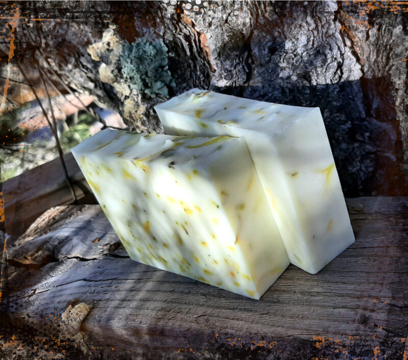 Two bars of pale yellow soap, each dotted with bright yellow calendula petals.