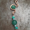 A string of teal-green and very pale blue beads hangs from a length of copper wire that's been bent into meandering curves. Another green bead is tucked into one of the curves.