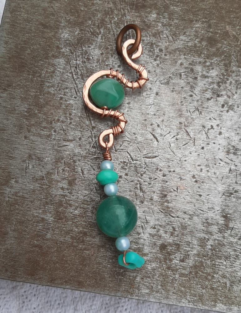 A string of teal-green and very pale blue beads hangs from a length of copper wire that's been bent into meandering curves. Another green bead is tucked into one of the curves.