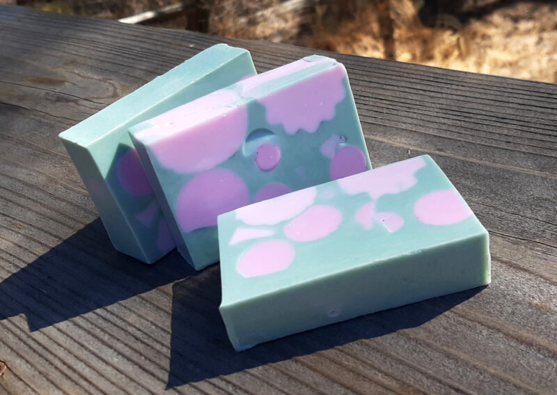 Three bars of green soap, each dotted with round pink bits.