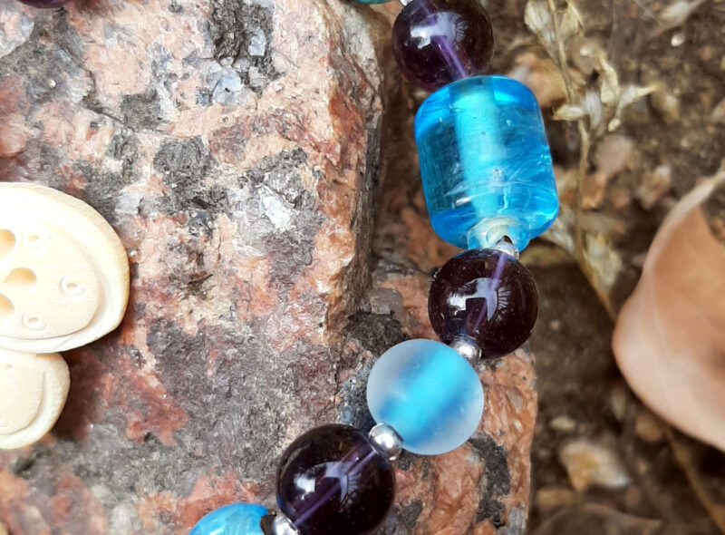 A close view of some of the beads. They alternate between teal and purple; most are spheres, but one slightly larger teal one is a cylinder. Tiny silver-colored beads separate the larger ones.