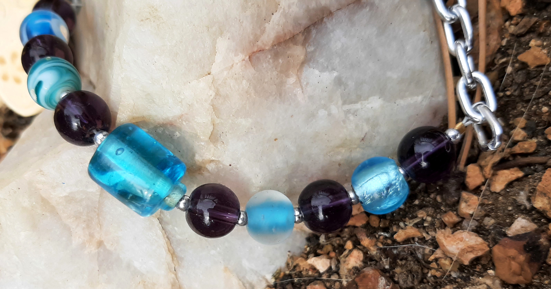 A close view of some of the beads. They alternate between teal and purple; most are spheres, but one slightly larger teal one is a cylinder. Tiny silver-colored beads separate the larger ones.